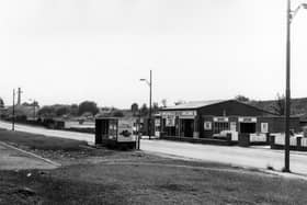 Stanningley Road from near the junction with Fairfield Mount, showing P.K. Motors garage on the far side of the road with the railway embankment behind. a bus shelter is seen on the near side. Pictured in July 1983.
